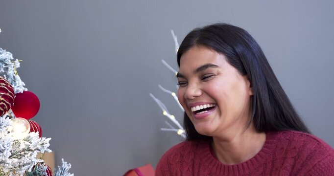 Woman reacting offcamera laughing then smiling beside frosted tree and presents in maroon sweater