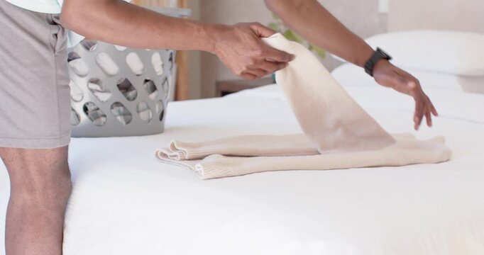 Man is reaching into basket, folding and tucking beige towel on white bedspread for storing