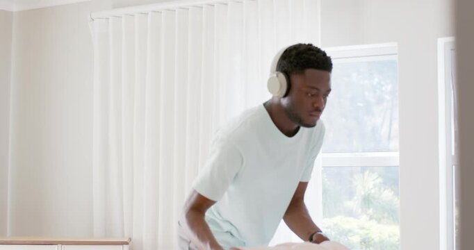 Man in mint tee holding linens, moving to laundry bin, inspecting and depositing garments by window