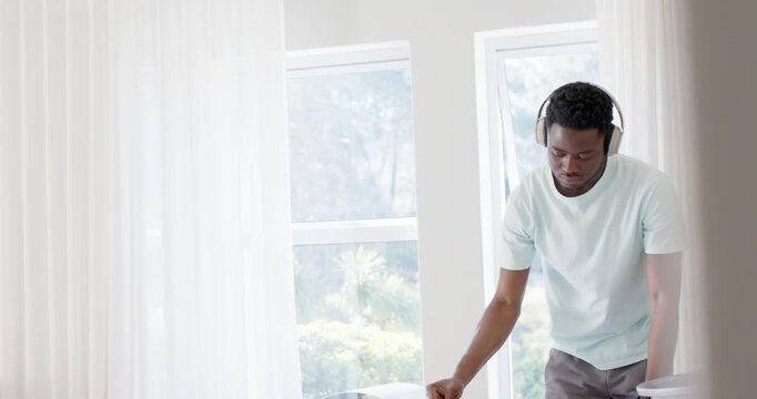 African American man holding and shaking gray sweatshirt, folding on bed into basket organizing