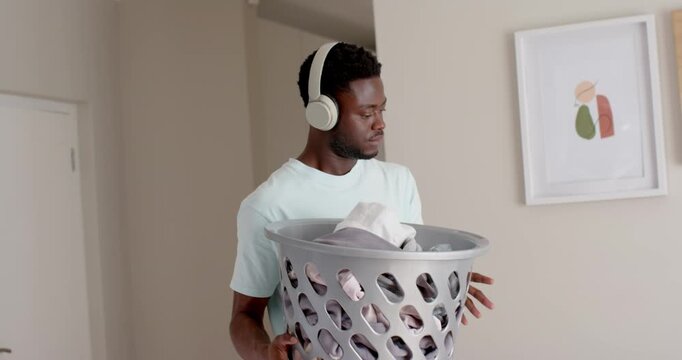 African American man entering apt holding gray basket, sitting on couch folding shirts to organize