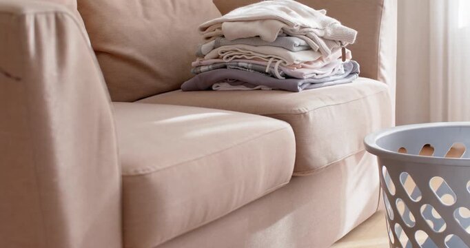 Camera is panning beige sofa with folded laundry near window as daylight is shifting conveying calm