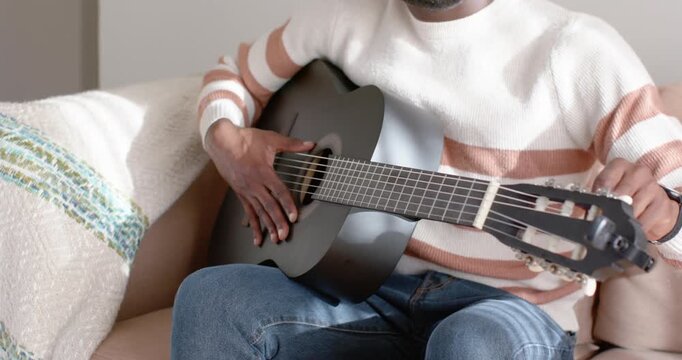 Hands are plucking strings and tuning pegs on black guitar on couch after hearing wrong note