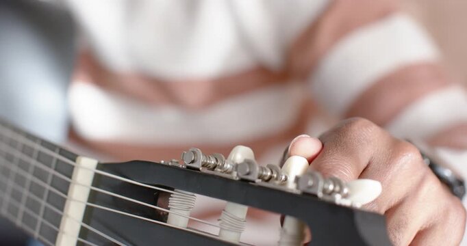 Right hand is reaching and turning white tuning pegs on guitar headstock, tuning strings