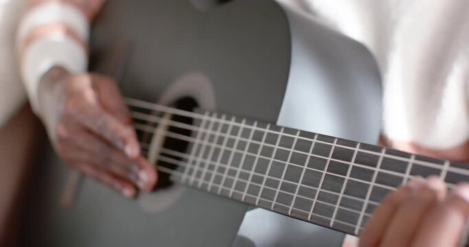 Hands are starting to pluck black guitar strings, forming chords and sliding on couch practicing