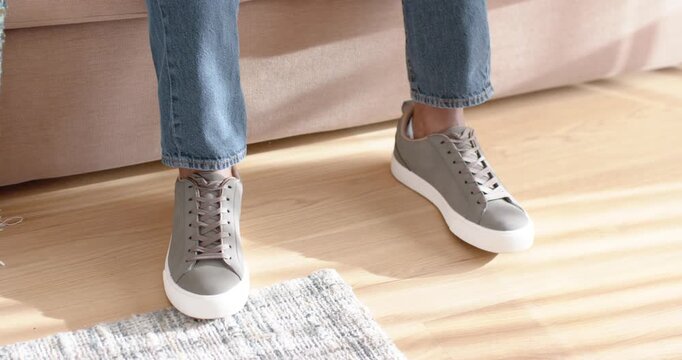Gray sneakers are shifting to adjust posture after sitting on beige sofa, sunlight striping floor