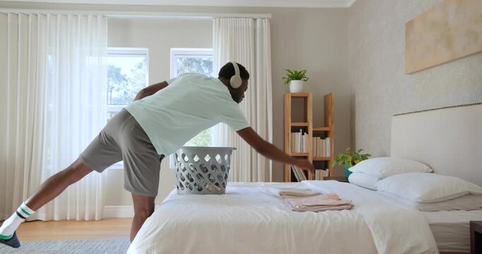 African American man pulling clothes from gray laundry basket folding on bed organizing linens