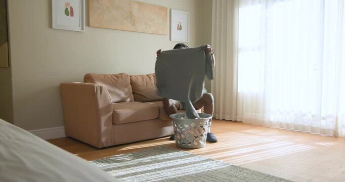 African American man carrying laundry basket at home, folding clothes on sofa to sort laundry