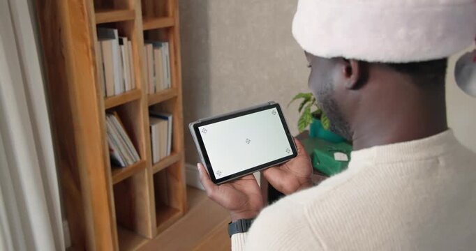 African American man in Santa hat holding tablet inspecting display markers, tilting
