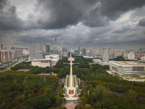 Aerial view of Century Park featuring lush green trees, a long central walkway, and modern skyscrapers under a dramatic cloudy sky in Shanghai, Shanghai, China.