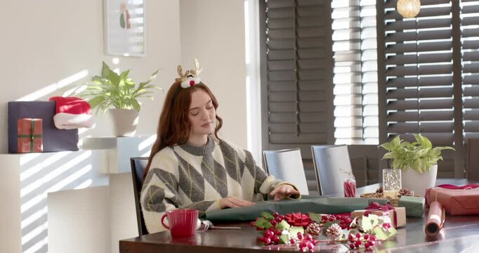 Woman sitting at table in argyle sweater, holiday spirit driving wrapping with green paper, ribbon