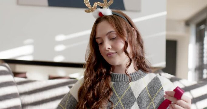 Woman on couch wearing reindeer headband and argyle upon inspecting ribbon pulling and forming bow