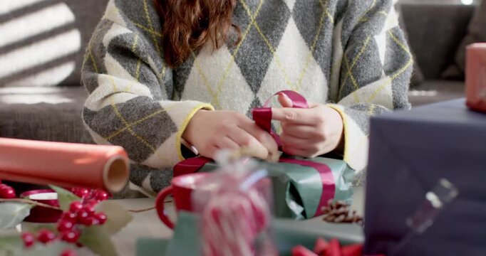 Person is placing red ribbon across green-wrapped box, then threading ends and shaping bow for gift