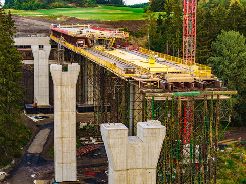 Aerial view of Lezky bridge construction site with concrete pillars, scaffolding, and a tall crane set against a rural forest landscape in Lubenec, Usti nad Labem Region, Czechia.