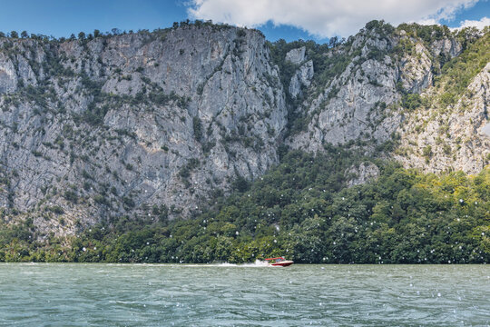 Speedboat navigating through the scenic Iron Gates gorge on the Danube River, surrounded by towering, forested mountains and a clear sky