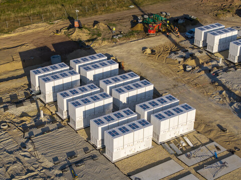 Aerial view of a Battery Energy Storage System construction site featuring rows of white storage containers, construction equipment, and workers in Poland.
