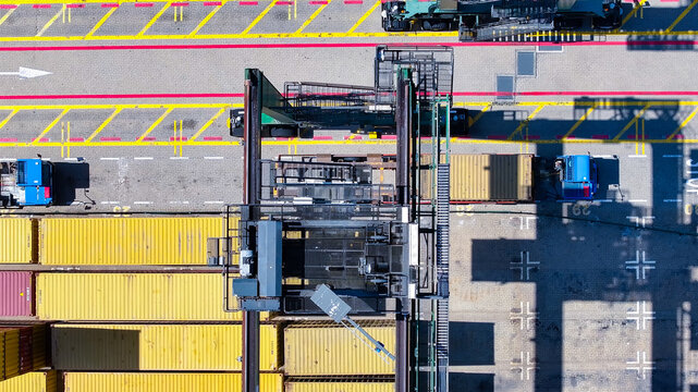 Aerial view of the Sines container port featuring rows of stacked yellow shipping containers, a large gantry crane, and trucks on the terminal pavement in Sines, Setubal, Portugal.