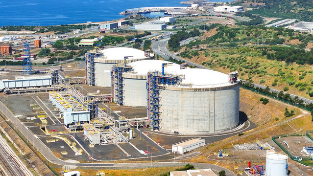 Aerial view of large oil storage tanks at an industrial petroleum terminal with complex piping infrastructure and surrounding green hills in Sines, Setubal, Portugal.