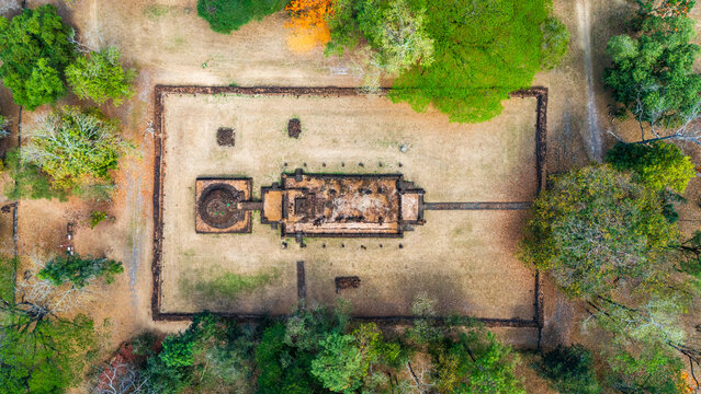 Aerial view of the ancient temple ruins at Si Satchanalai Historical Park, featuring stone structures surrounded by lush trees and dry grounds in Si Satchanalai, Sukhothai, Thailand.
