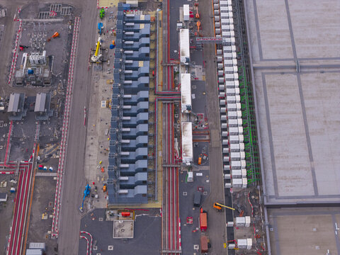 Aerial view of a hyperscale data center featuring rows of cooling units, complex piping infrastructure, and large industrial buildings in Belgium.