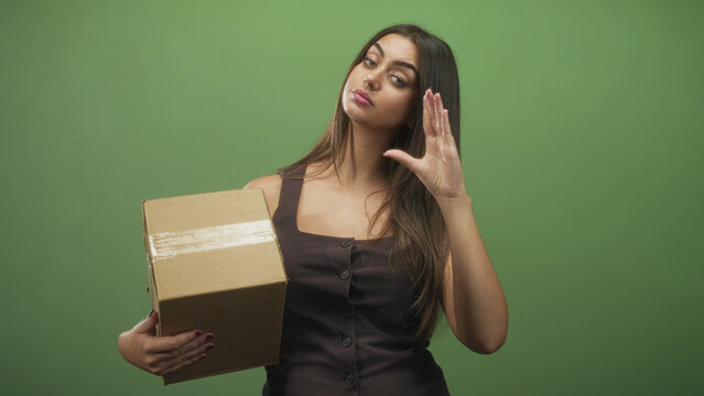Woman holding cardboard box with one hand and hand raised in a dismissive flick gesture in studio; indifference delivery logistics.