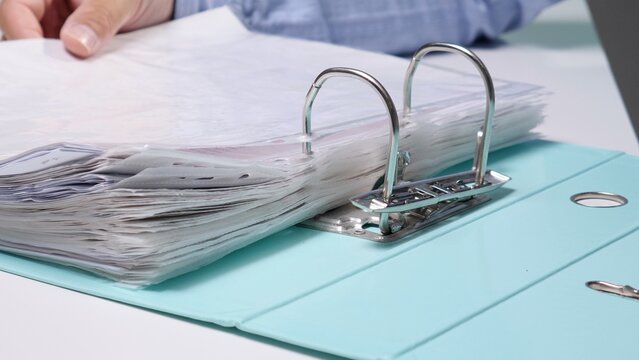 Person's hand opening a full ring binder, organizing and archiving important business documents, paperwork, and financial records in an office setting