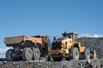 Yellow Wheel Loader and Orange Dump Truck Parked at Quarry Worksite © HansMorten