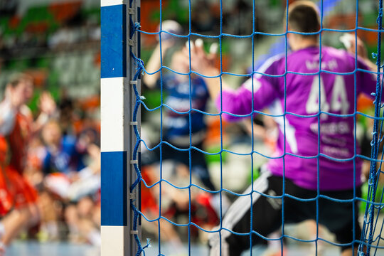 Handball goalpost and blurred goalkeeper and forward during indoor match with blurred players, capturing sports action and competitive atmosphere