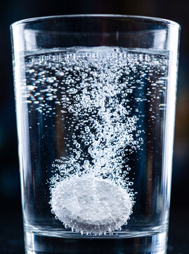 Effervescent tablet dissolving in a glass of clear water creating bubbles