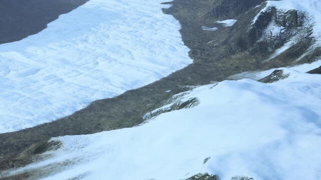 A large area of snow near rocky hills. The snow covers parts of the ground, and there are patches where the land is visible. The photo captures a glacier and the surrounding terrain.