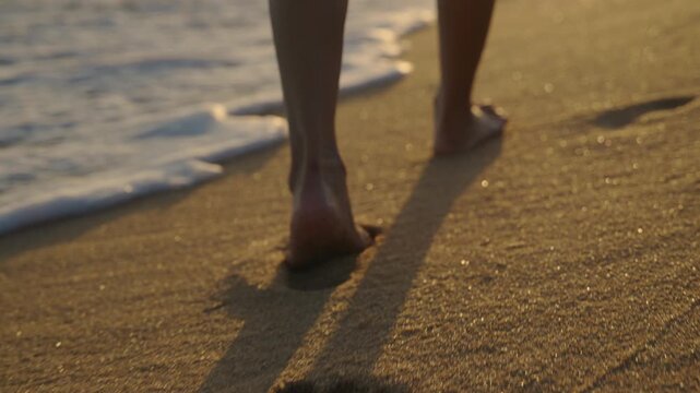 Closeup of bare feet of woman walking on beach sand at sunset, travel lifestyle concept showing girl strolling along sea shore with ocean waves during warm golden hour.