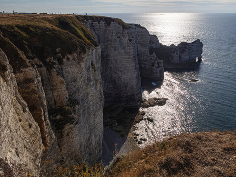 Vista de los acantilados de Etretat en la Normand&iacute;a de Francia desde arriba, con el sol reflejado en el agua del mar y las monta&ntilde;as a contraluz , viajando en verano de 2022