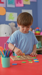 Naklejka premium Boy placing wooden puzzle shapes with fingers and hands on a red kids table surrounded by colored pencils and toys in a bright studio; concentration learning.