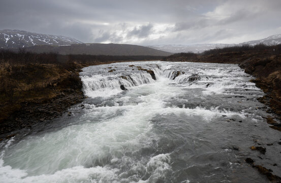 Waterfall flow over rocks in a river mountains and cloudy sky. Bruarfoss waterfall Iceland