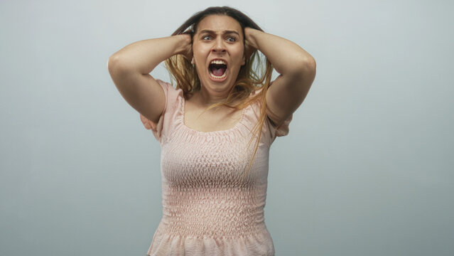 Woman in pink dress pulls hair with hands on head in studio, mouth open screaming; frustration meltdown.