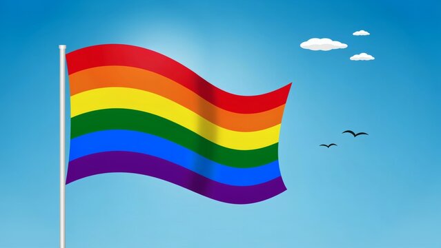 A vibrant rainbow pride flag waving on a pole against a clear blue sky background with attached flagpole ripples ripples breeze under small clouds birds