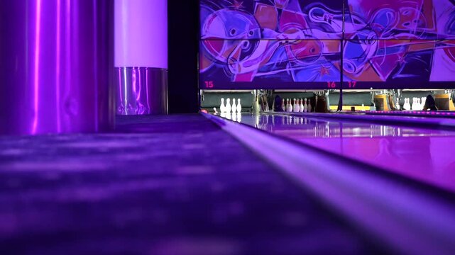 Pink bowling ball striking pins on a purple lit lane