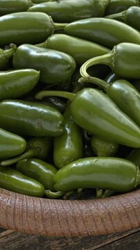 Jalape&ntilde;o peppers heap close-up on a handmade dish. A brown plate of fresh green chilies on a dark, rustic wooden background. Table spin, vertical video.