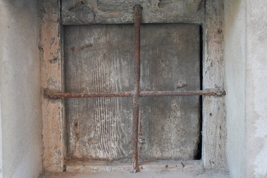 Rusty iron cross bars over aged wooden window in an old building