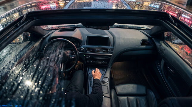 High angle view of a person driving a luxury convertible car with open roof on a rainy night in the city