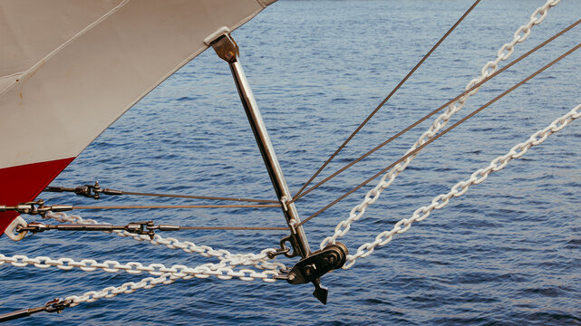 A close-up shot of a ship bow with white rigging chains and metal ropes over blue sea water during a sunny day.