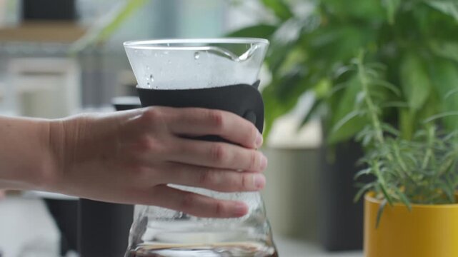 Woman removes coffee dripper with filter from glass server and swirls brewed coffee by hand. Concept of pour over coffee preparation