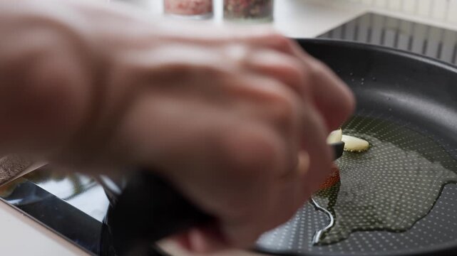 Woman removes fried garlic cloves from hot oil in frying pan. Preparing garlic flavored oil and ingredients for meal
