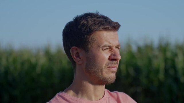 Man closes his eyes and squints as bright sunlight hits his face near field. Concept of strong sun glare and eye discomfort outdoors