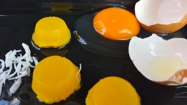 Egg yolk, molded yellow desserts, *quindim* and grated coconut, eggshell on a kitchen surface.