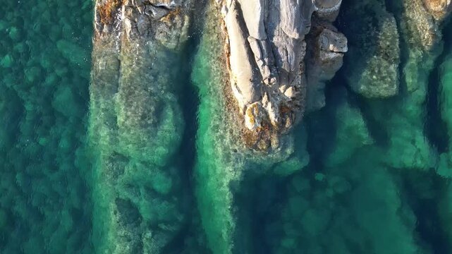 Aerial drone view pulling back over clear turquoise sea water and rocky coast of Ospedaletti near Sanremo, Italian Riviera
