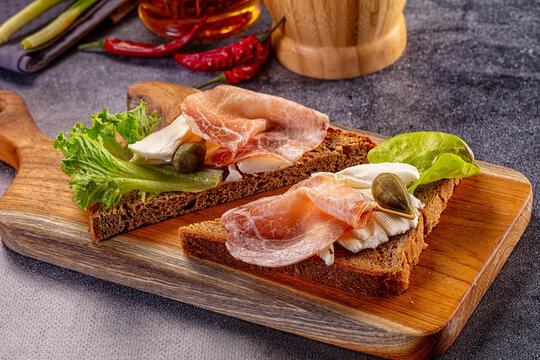 Open faced sandwich with prosciutto cheese lettuce and caper on wooden board