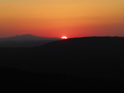 Aerial view of the sun setting behind rolling hills in the landscape of Spoleto, Umbria, Italy.