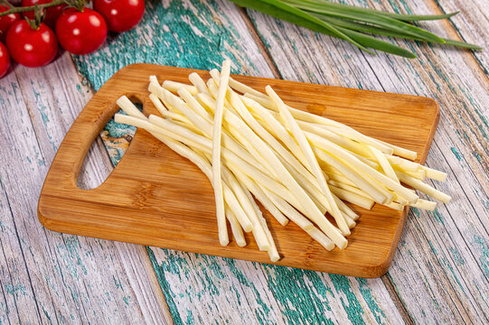 String cheese sticks on wooden cutting board with cherry tomatoes and green onions