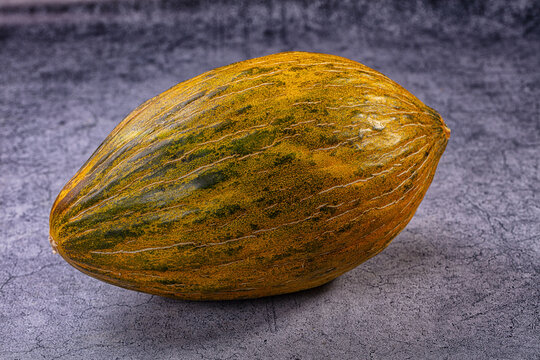 Whole piel de sapo melon on textured gray background with natural lighting and shallow depth of field